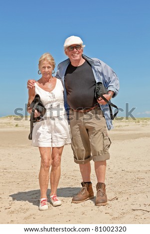 Senior couple standing on empty beach under clear blue sky on hot summer day.