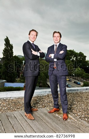 Two young business outdoors on top of building with cloudy sky.