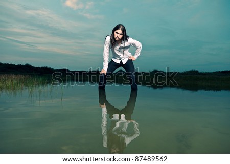 Young casual tough man with long hair and beard standing in lake