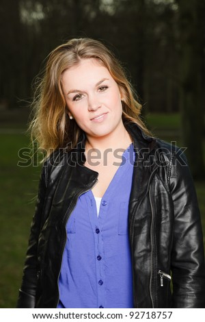 Pretty young woman long blond hair in winter forest wearing black leather jacket and blue shirt