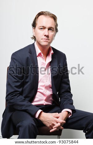Young business man with blond hair in blue suit and pink shirt serious looking isolated on white background