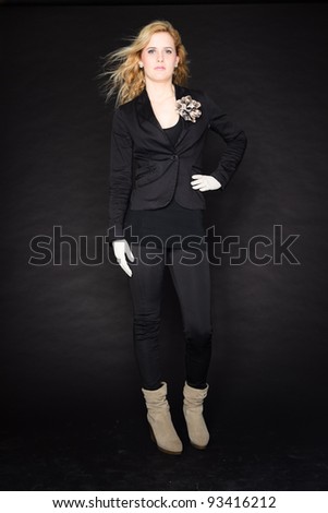 Studio portrait of pretty young woman with pink lipstick and long blond hair. Wearing a black suit and white gloves. Isolated on black background.