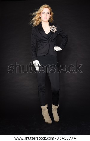 Studio portrait of pretty young woman with pink lipstick and long blond hair. Wearing a black suit and white gloves. Isolated on black background.