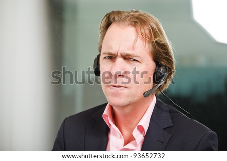 Young business man blond hair with headset wearing blue suit and pink shirt