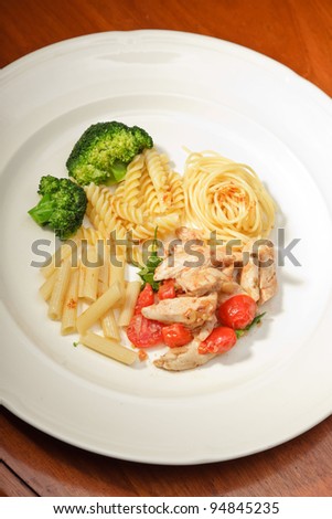 Dinner of vegetables pasta tomato and chicken on a white plate and wooden table