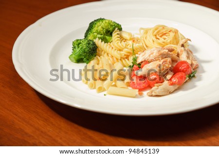 Dinner of vegetables pasta tomato and chicken on a white plate and wooden table