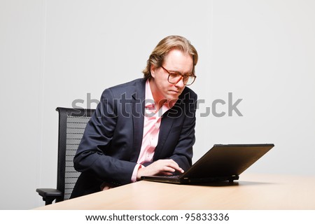 Young business man blond hair working with laptop isolated on white background. Wearing glasses blue suit and pink shirt.