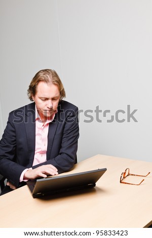 Young business man blond hair working with laptop isolated on white background. Wearing blue suit and pink shirt.
