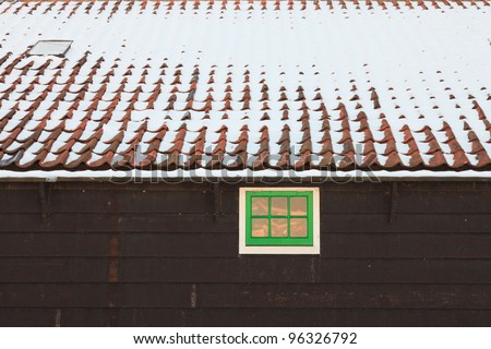 Roof of wooden house with green window covered with snow. Old dutch village de Zaanse Schans.