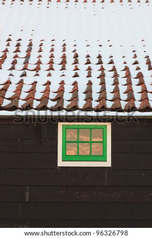 Roof of wooden house with green window covered with snow. Old dutch village de Zaanse Schans.