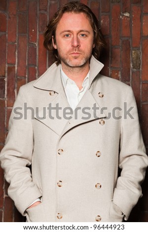 Casual man long hair white jacket standing in front of brick wall