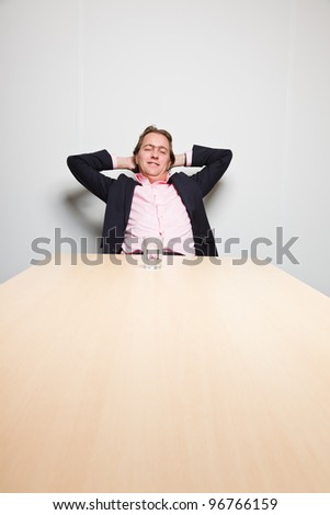 Business man with blond hair sitting bored behind table in boardroom isolated on white background