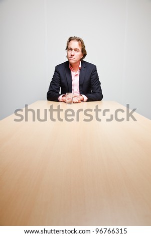 Business man with blond hair sitting bored behind table with glass of water in office isolated on white background