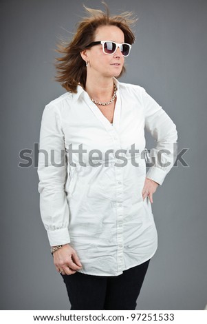 Studio portrait of middle aged woman with sunglasses and white shirt isolated on grey background