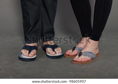 Feet of man and woman wearing flip-flops isolated on grey background.