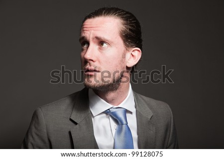 Sad business man brown long hair with expressive face wearing grey suit and blue tie. Isolated on grey background.