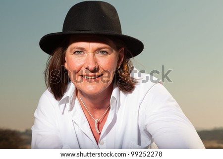 Attractive confident woman wearing a hat middle aged enjoying outdoors. Clear sunny spring day with blue sky.