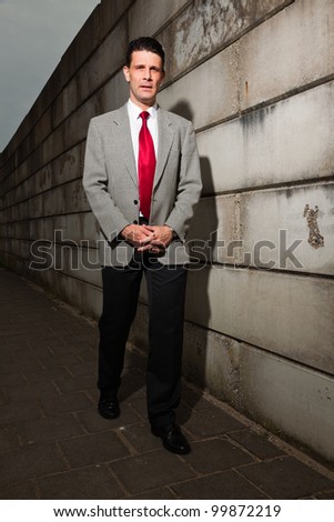 Business man with grey suit and red tie walking on the street near brick wall. Industrial environment.