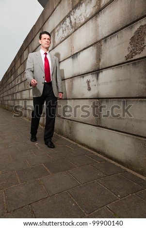 Business man with light grey suit and red tie walking on the street near brick wall. Industrial environment.