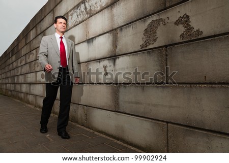 Business man with grey suit and red tie walking on the street near brick wall. Industrial environment.