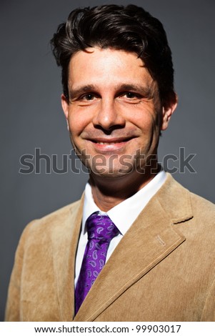 Smiling business man with light brown suit and purple tie isolated on dark background. Studio shot.