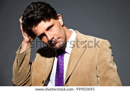 Confused business man with light brown suit and purple tie isolated on dark background. Studio shot.