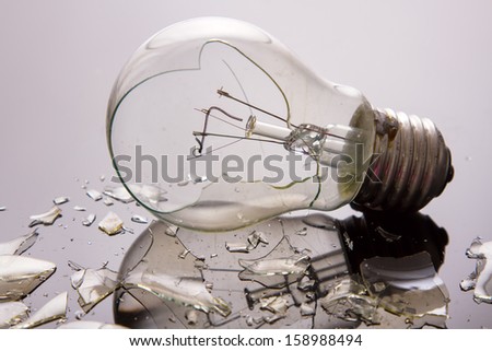 Broken light bulb on shiny surface with pieces backlit