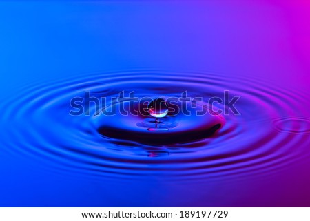 Water drop close up with concentric ripples on colourful blue and pink surface