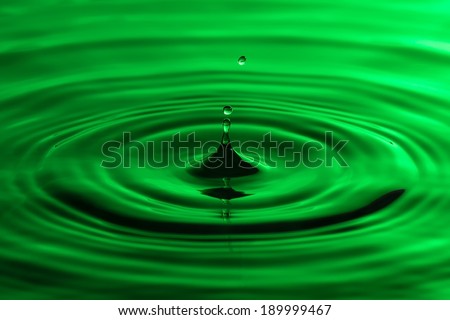 Water drop close up with concentric ripples on colourful green surface