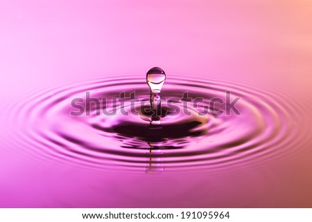 Water drop close up with concentric ripples on colourful pink and yellow surface