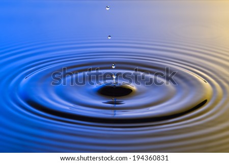 Water drop close up with concentric ripples on colourful blue and yellow surface