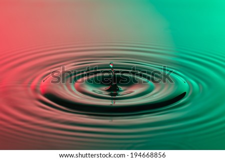 Water drop close up with concentric ripples on colourful red and green surface