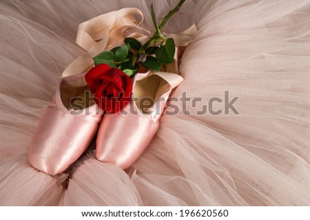 Old used ballet slippers lying on floor with rose and pink tutu