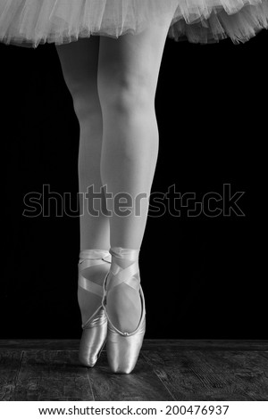 A ballet dancer standing on toes while dancing on black background