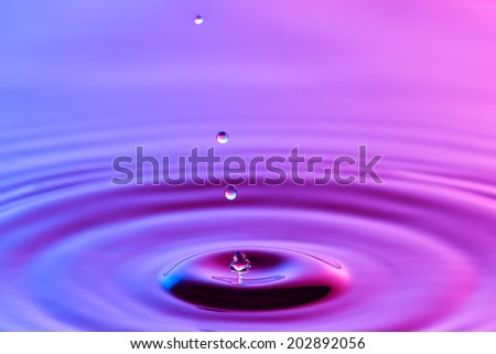 Water drop close up with concentric ripples on colourful blue and pink surface