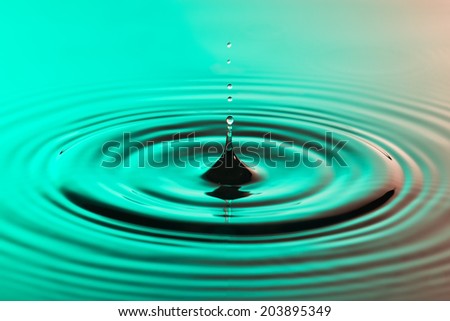 Water drop close up with concentric ripples on colourful pink and green surface