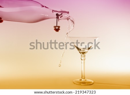 Clear water pour out of bottle splash into glass and spill with a pink and yellow back lighting
