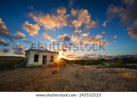 Old small deserted house in field with a cloud sunset landscape