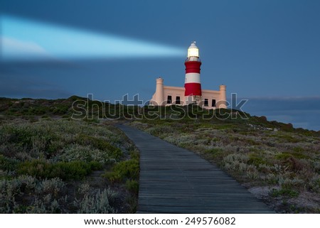 Lighthouse with shining light in darkness with dark blue clouds
