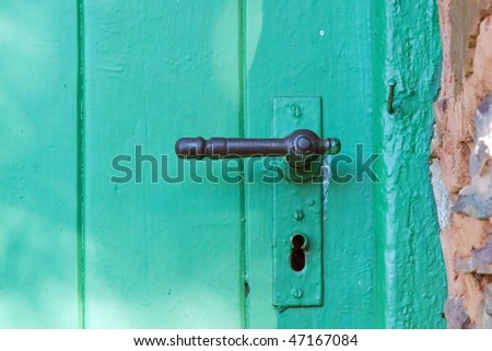 Old green door with worn iron handle in a rock wall