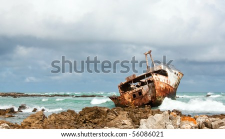 Rusting broken Shipwreck lying on the rocks with green ocean and cloudy sky