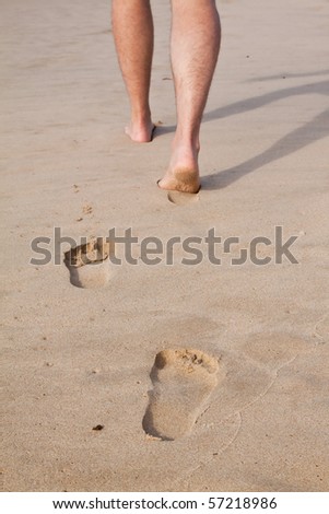 Footprints in wet sand in a line with a man walking on the beach