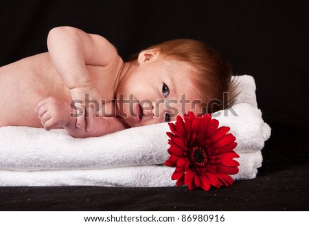 Baby girl lying on white towels with red flower folded in the towels