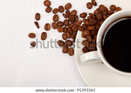 White cup, black coffee and brown coffee beans on a white table cloth