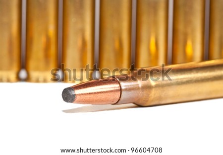 One bullet lying in front of a row of bullets on a white surface