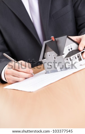 Real estate concept - business man signs contract behind household architectural model