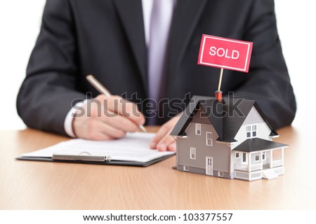 Real estate concept - business man signs contract behind house architectural model