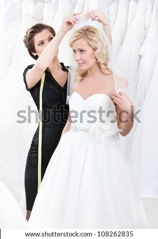 Shop assistant helps to the bride to fix the wedding veil