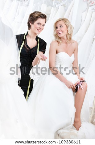Shop assistant gives some piece of advice while future bride in wedding gown puts the garter