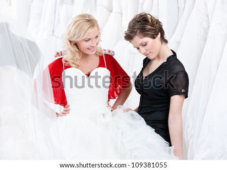 Young girl is thinking over a wedding gown.Shop assistant helps her